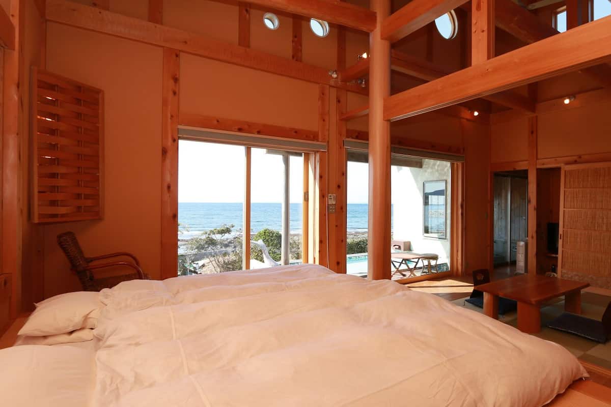 A wooden cabin with a large bed, a dining table, and a view of the ocean.