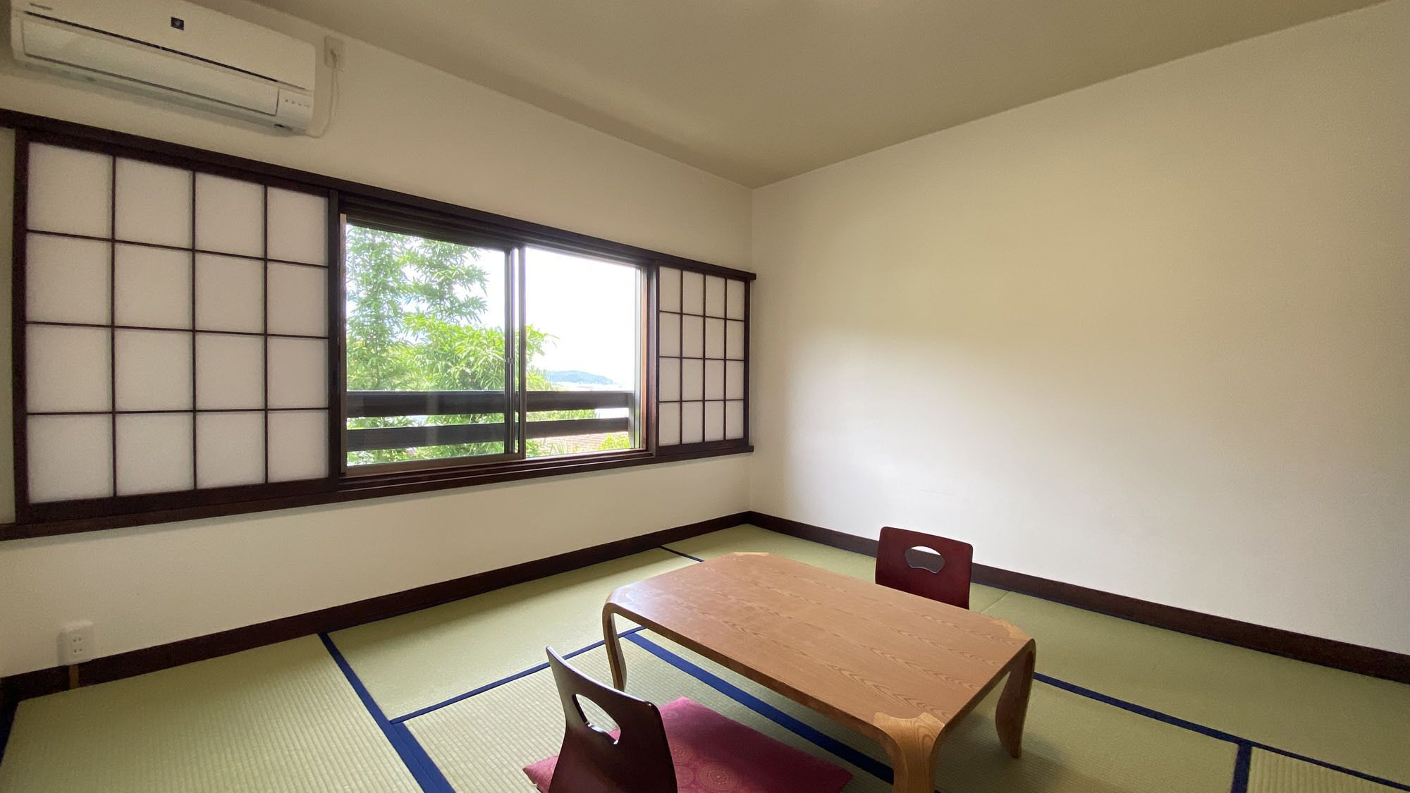 Une pièce dotée d’un sol recouvert de tatamis, d’une table basse, d’une chaise et d’un paravent en papier de riz (shoji) offrant une vue sur la verdure à l’extérieur.