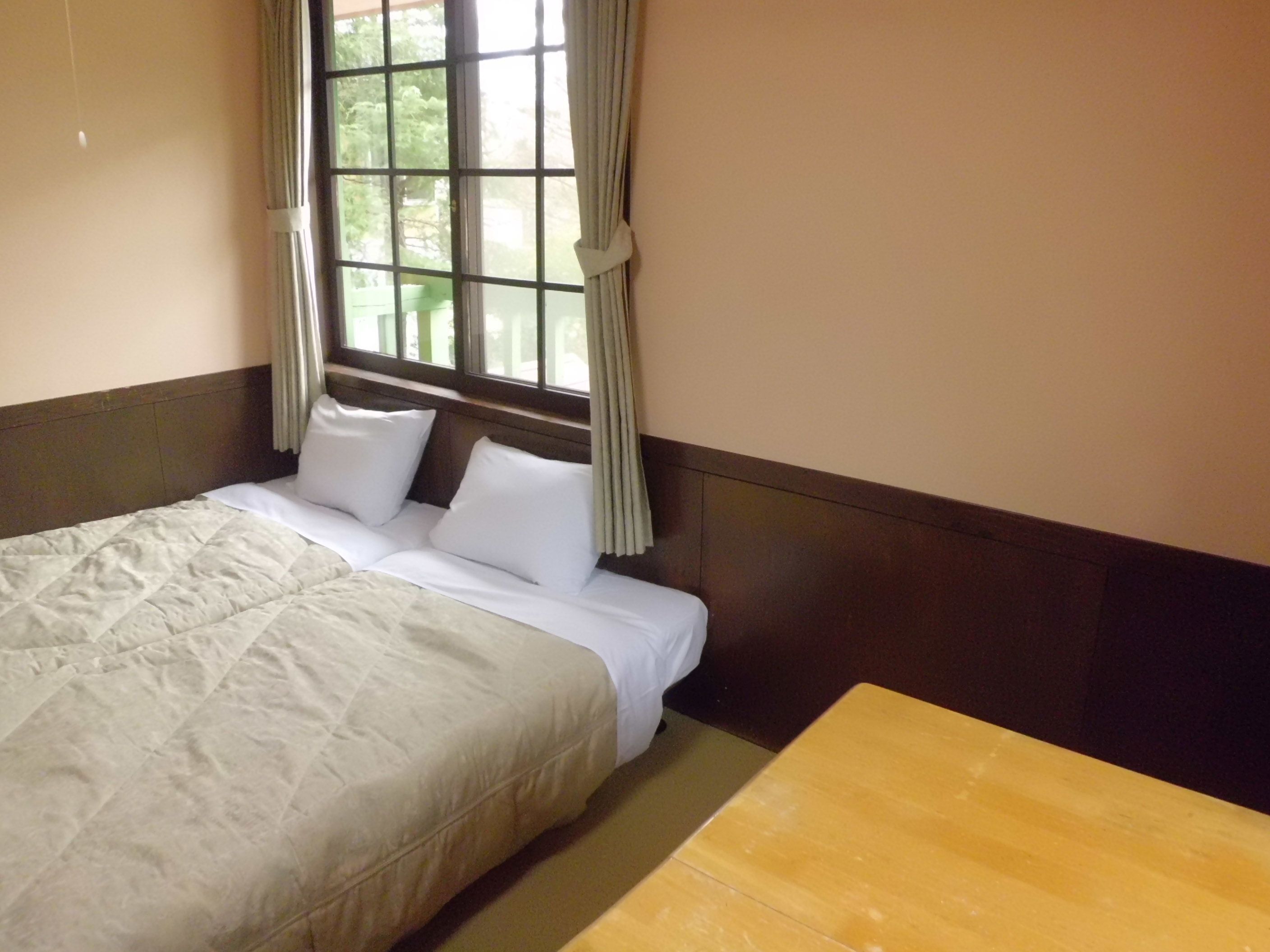 A hotel room with a bed, a wooden table, and a window with curtains.