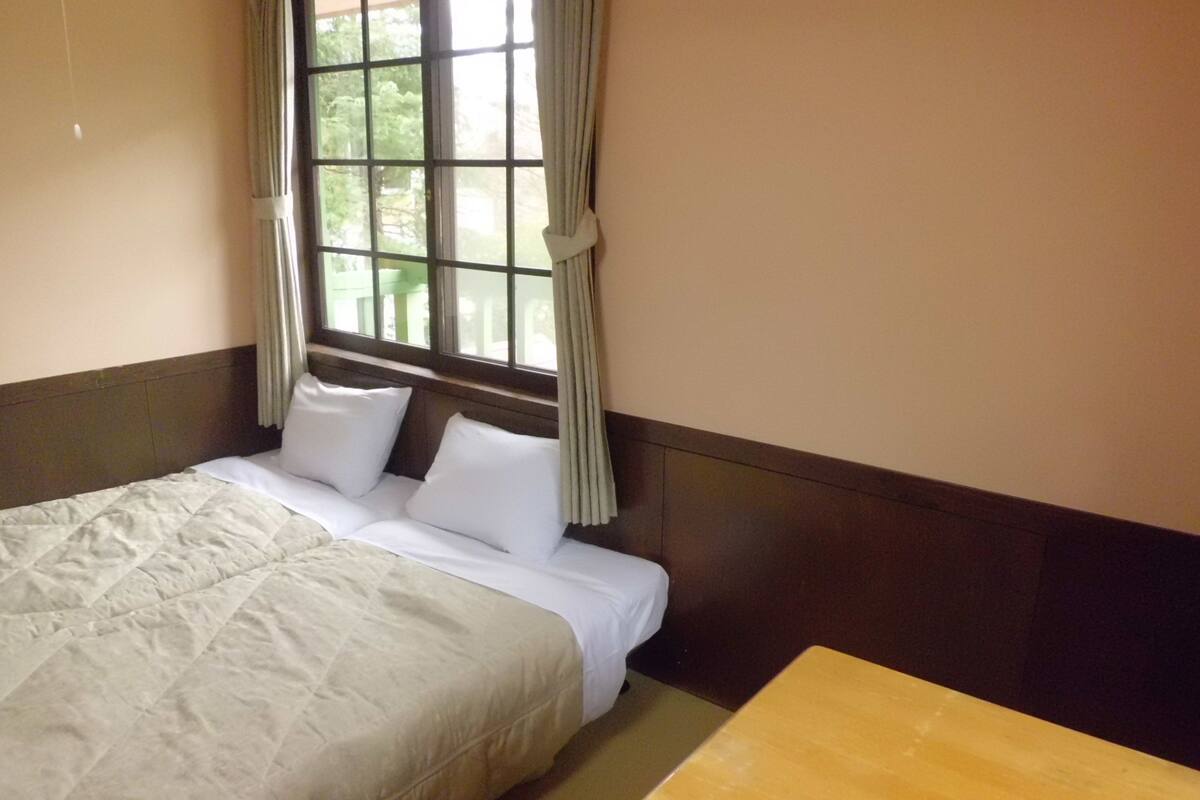 A hotel room with a bed, a wooden table, and a window with curtains.