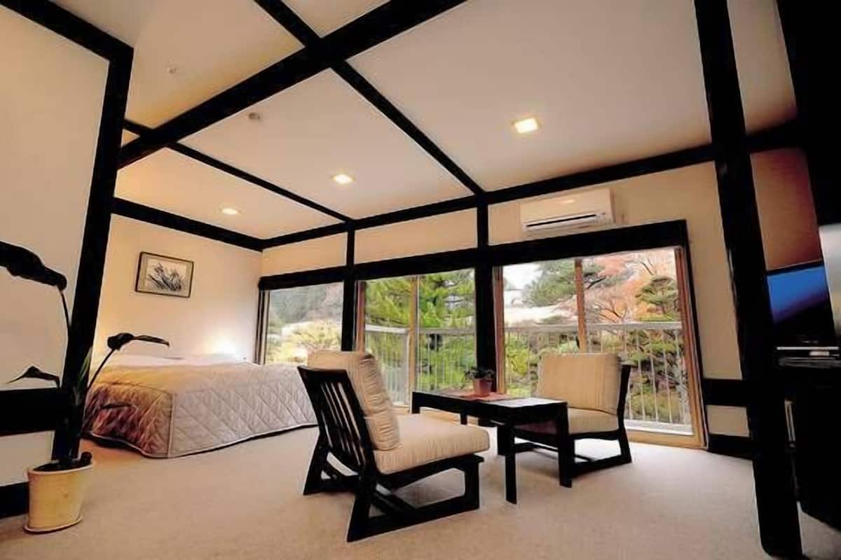 A bedroom with a bed, two chairs, a small table, and a TV.