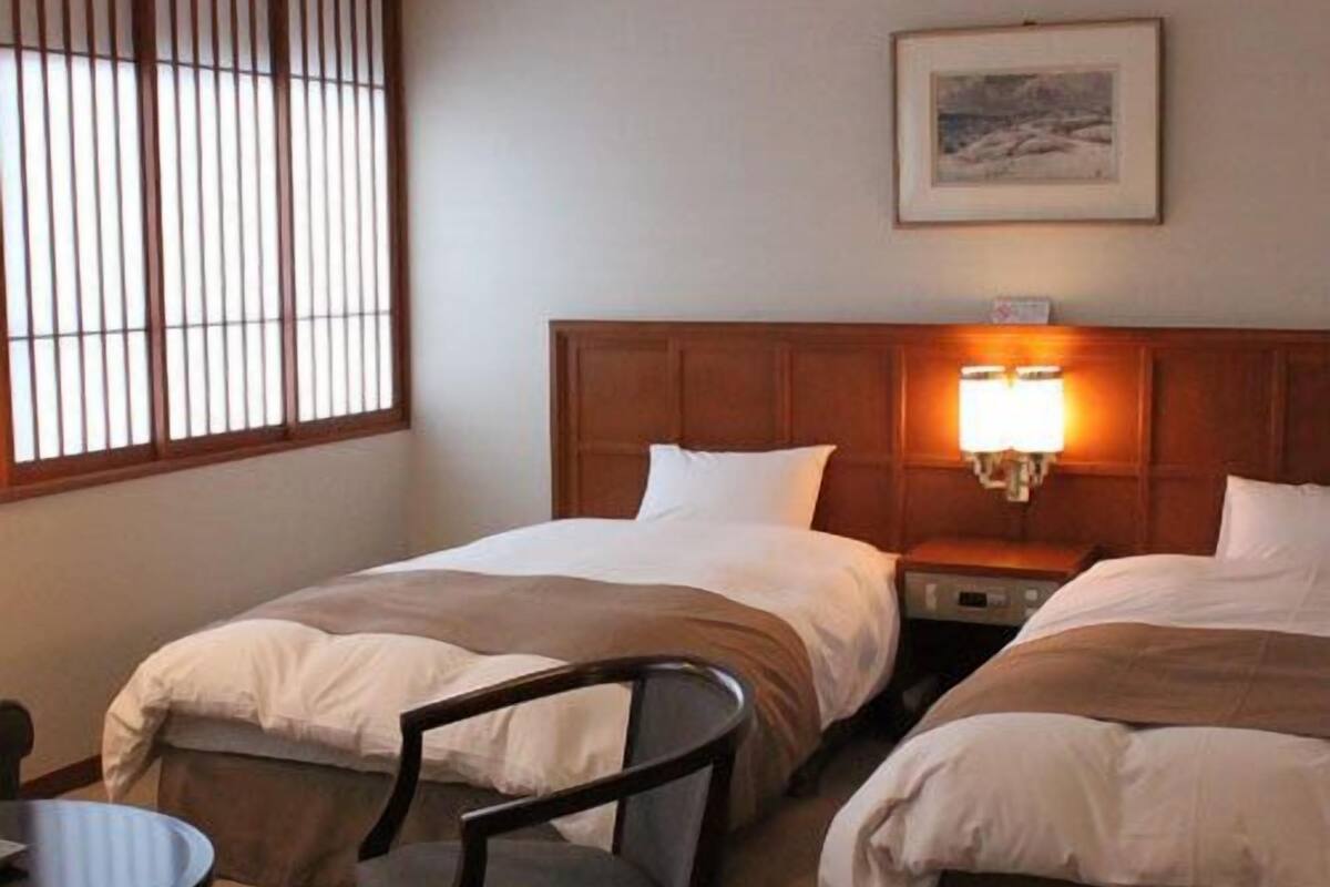 Une chambre d’hôtel avec deux lits, une chaise, une table et une lampe.