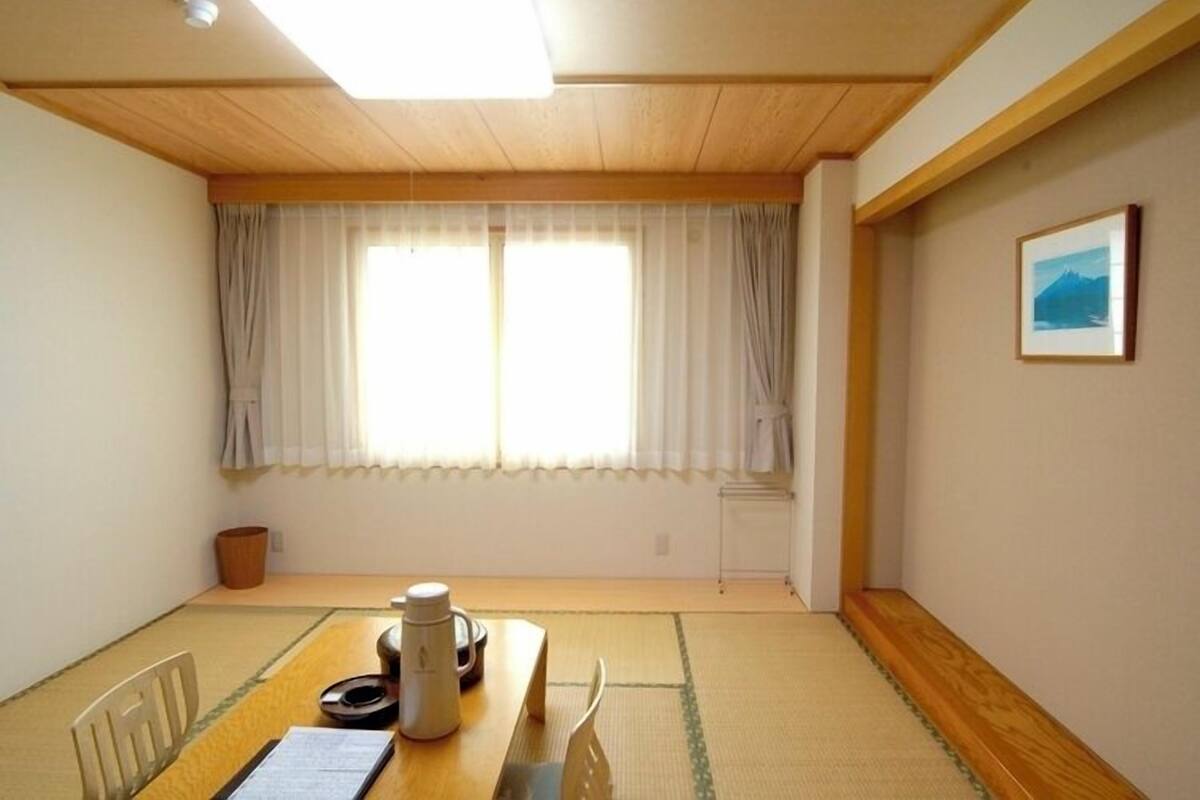 Une pièce avec un sol recouvert de tatamis, une table en bois avec une bouilloire, et un tableau encadré accroché au mur.