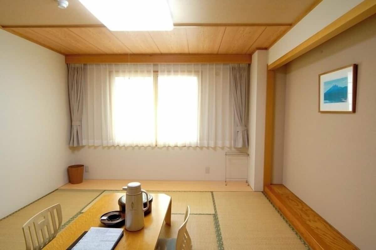 A room with a tatami mat floor, a wooden table with a kettle, and a framed picture on the wall.