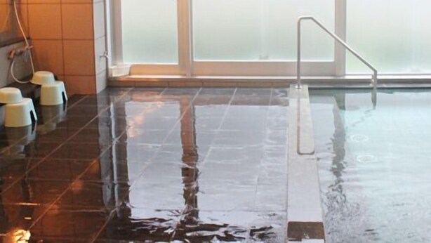 Una piscina interior amplia con paredes de vidrio transparente, suelo de baldosas y una escalera de metal.