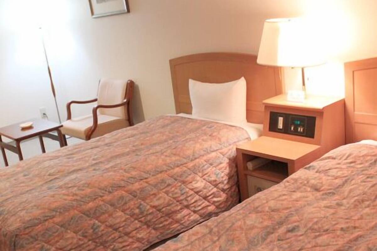 Une chambre d’hôtel avec deux lits, une table de chevet avec une lampe, une chaise et une petite table.