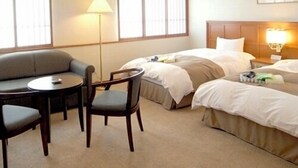 Una habitación de hotel con una cama, dos mesitas de noche, un sofá, un sillón y una lámpara.