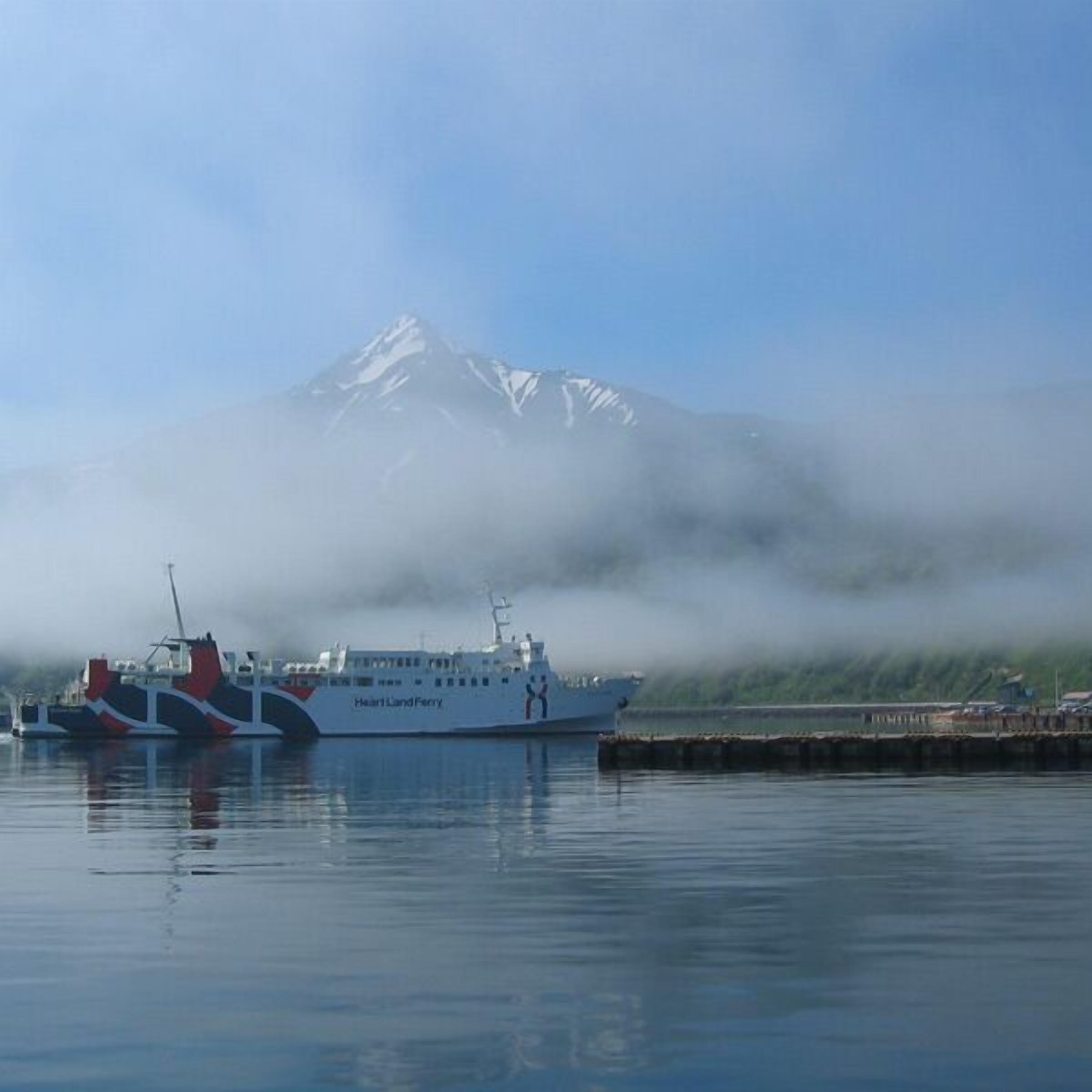 Færgen 'Heartland Ferry' ligger til kaj med et bjerg i baggrunden.