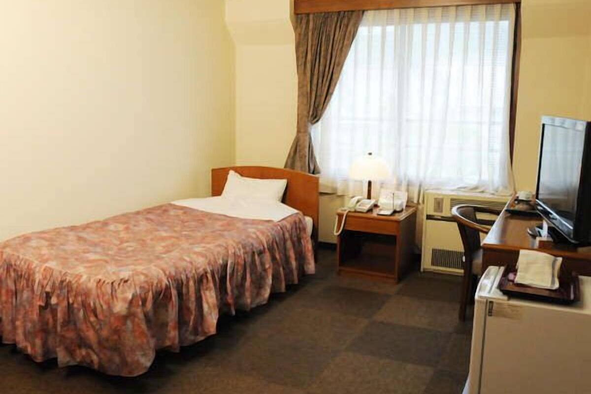 Ein Hotelzimmer mit einem Bett, einem Schreibtisch mit Computer, einem Fernseher und einem Fenster mit Vorhängen.