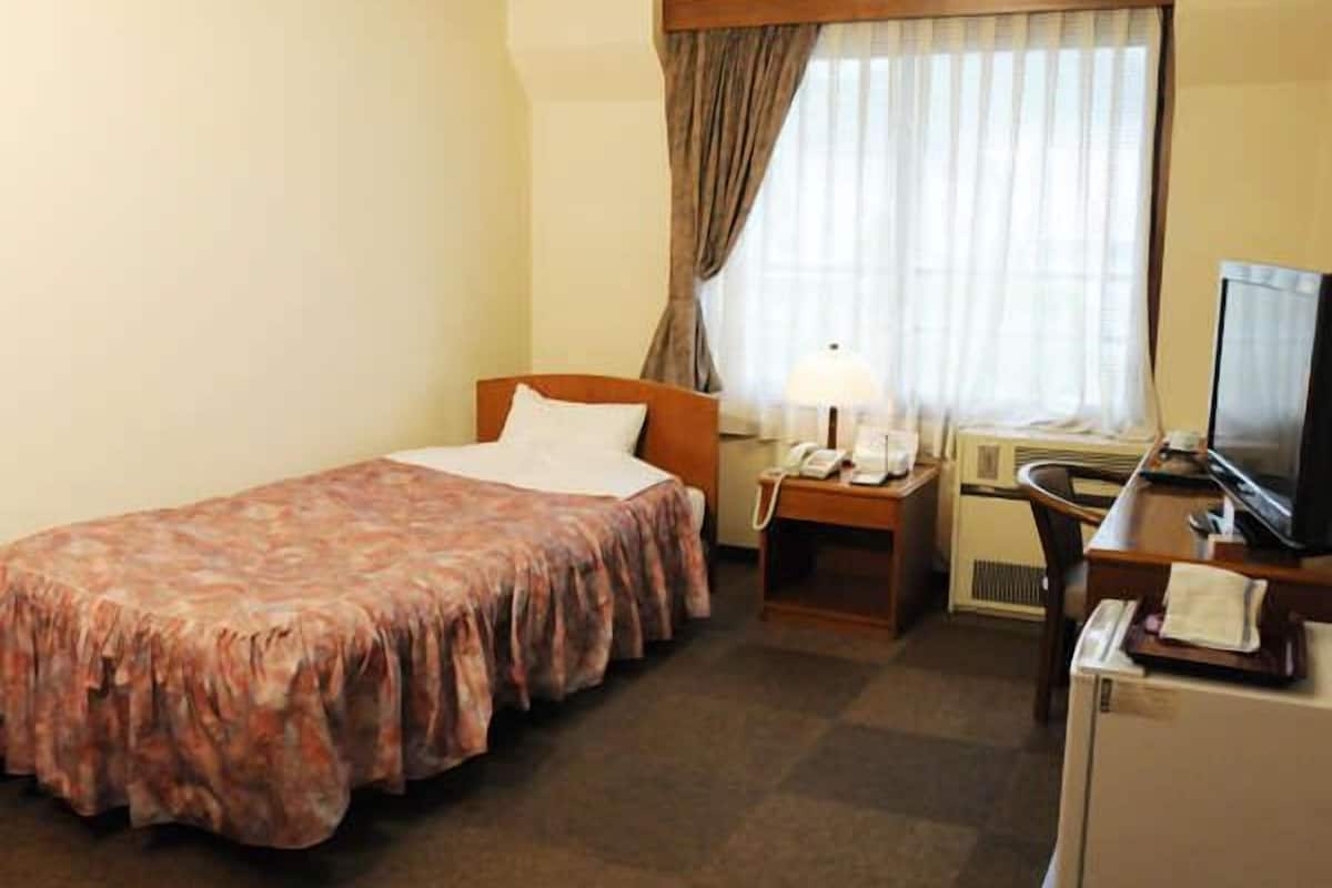 A hotel room with a bed, a desk with a computer, a television, and a window with curtains.