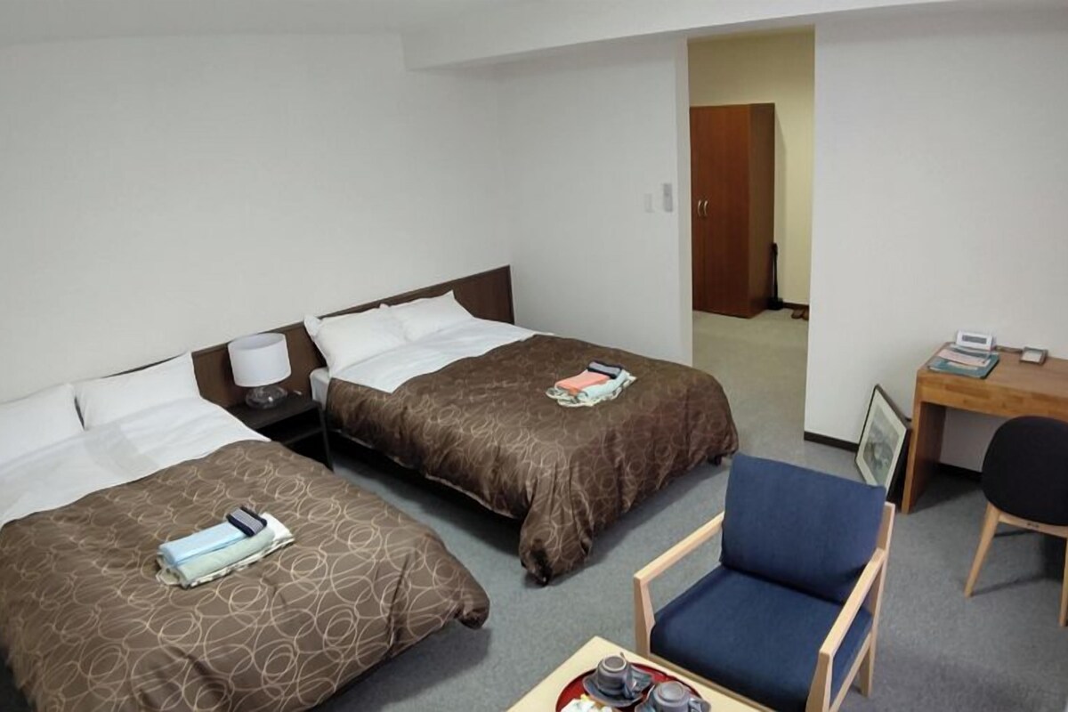 Ein Hotelzimmer mit zwei Betten, einem Schreibtisch, einem Sessel und einem kleinen Tisch mit Tablett.