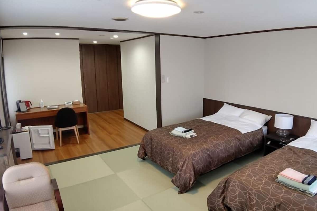 Ein Hotelzimmer mit zwei Betten, einem Schreibtisch, einem Sessel und einem Fernseher.