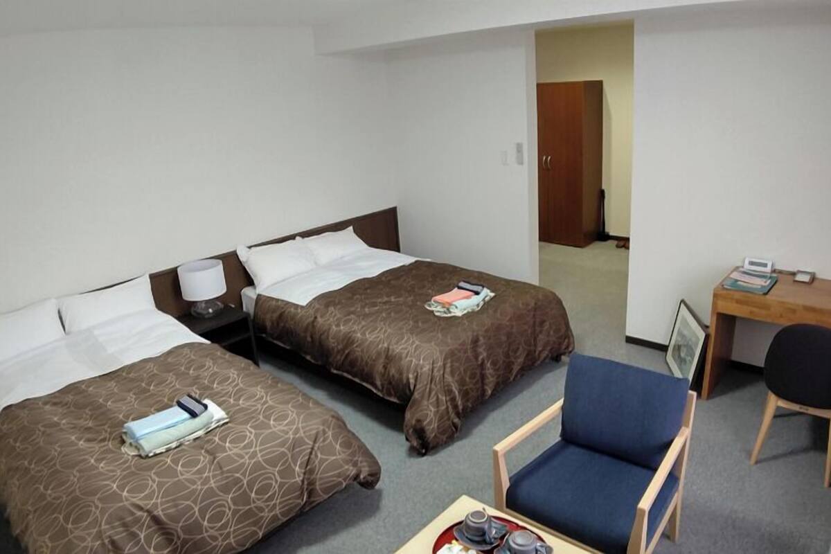 Ein Hotelzimmer mit zwei Betten, einem Schreibtisch, einem Sessel und einem kleinen Tisch mit Tablett.