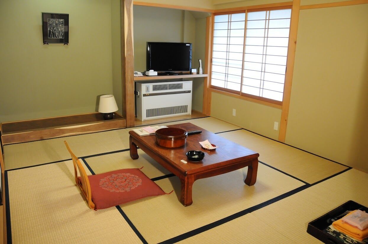 A traditional Japanese room with tatami flooring, a television, a heater, a wooden table, and a red mat.