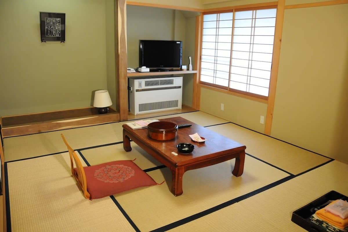 Ein traditioneller japanischer Raum mit Tatami-Boden, einem Fernseher, einem Heizgerät, einem Holztisch und einer roten Matte.