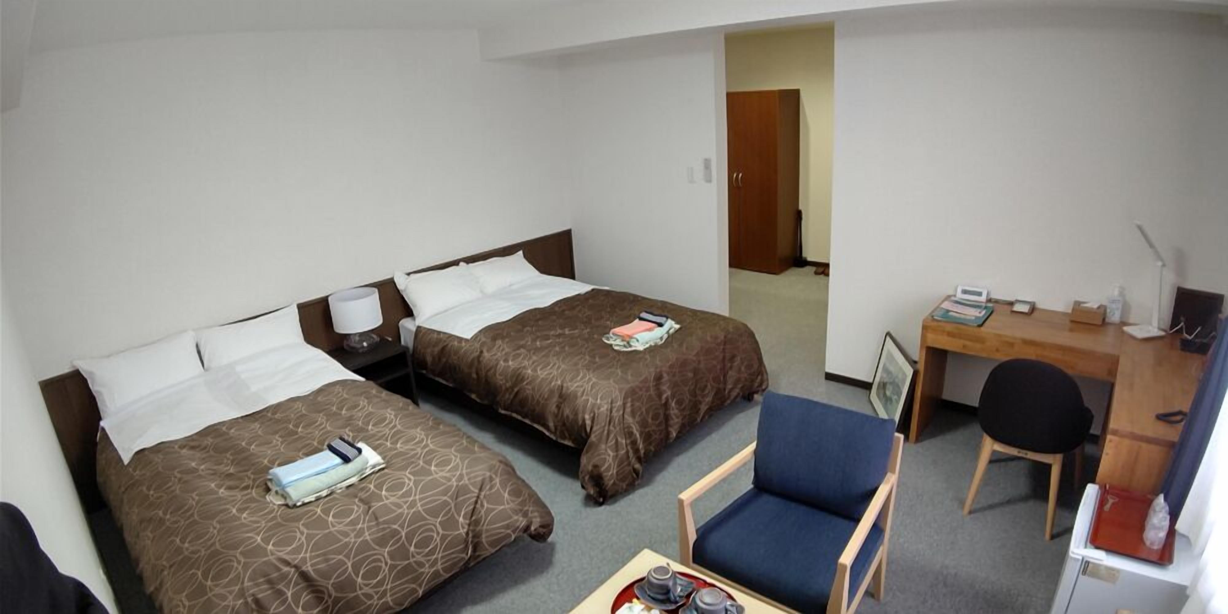 A hotel room with two beds, a desk, a chair, and a small table with a tray.