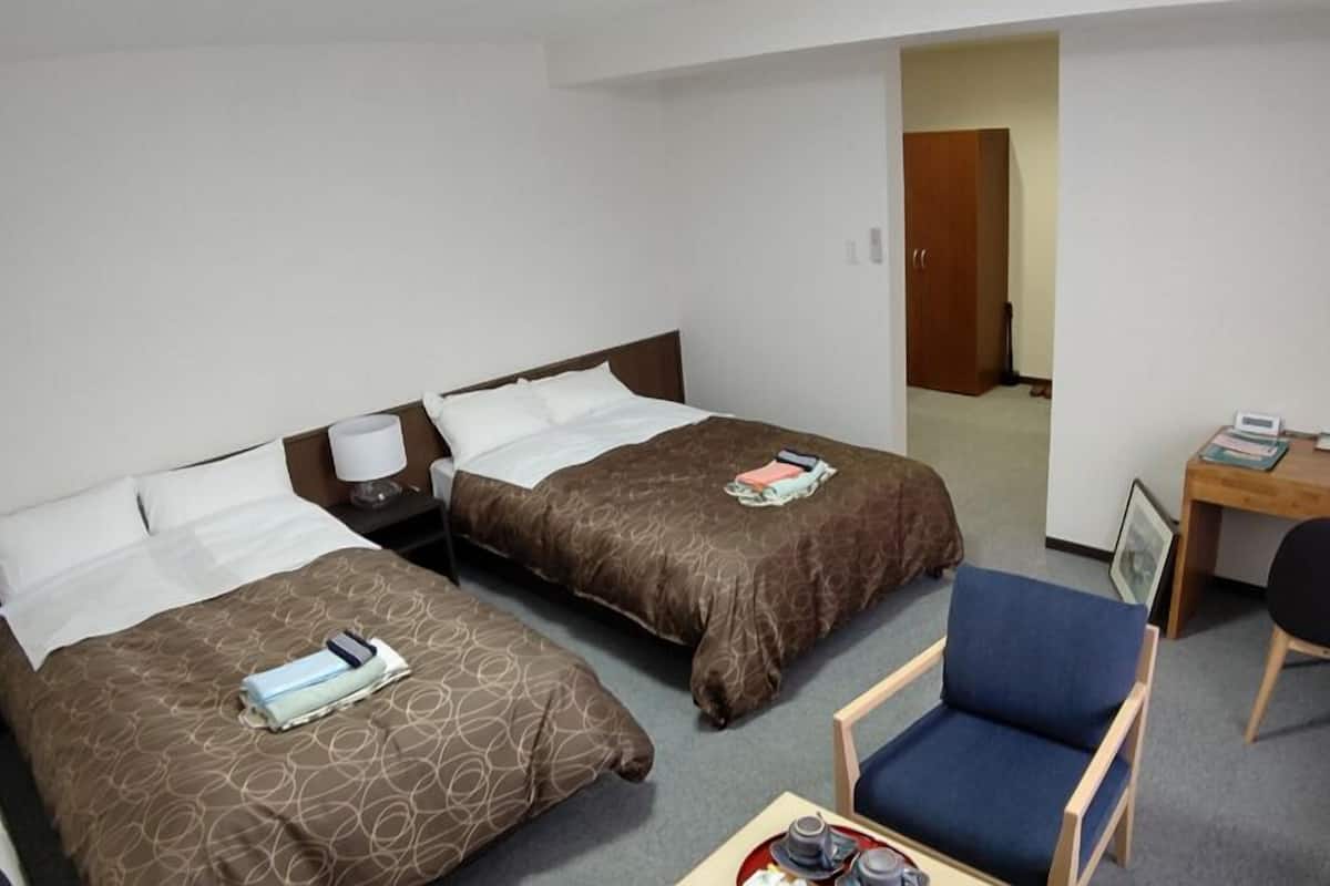 Ein Hotelzimmer mit zwei Betten, einem Schreibtisch, einem Stuhl und einem kleinen Tisch mit Tablett.