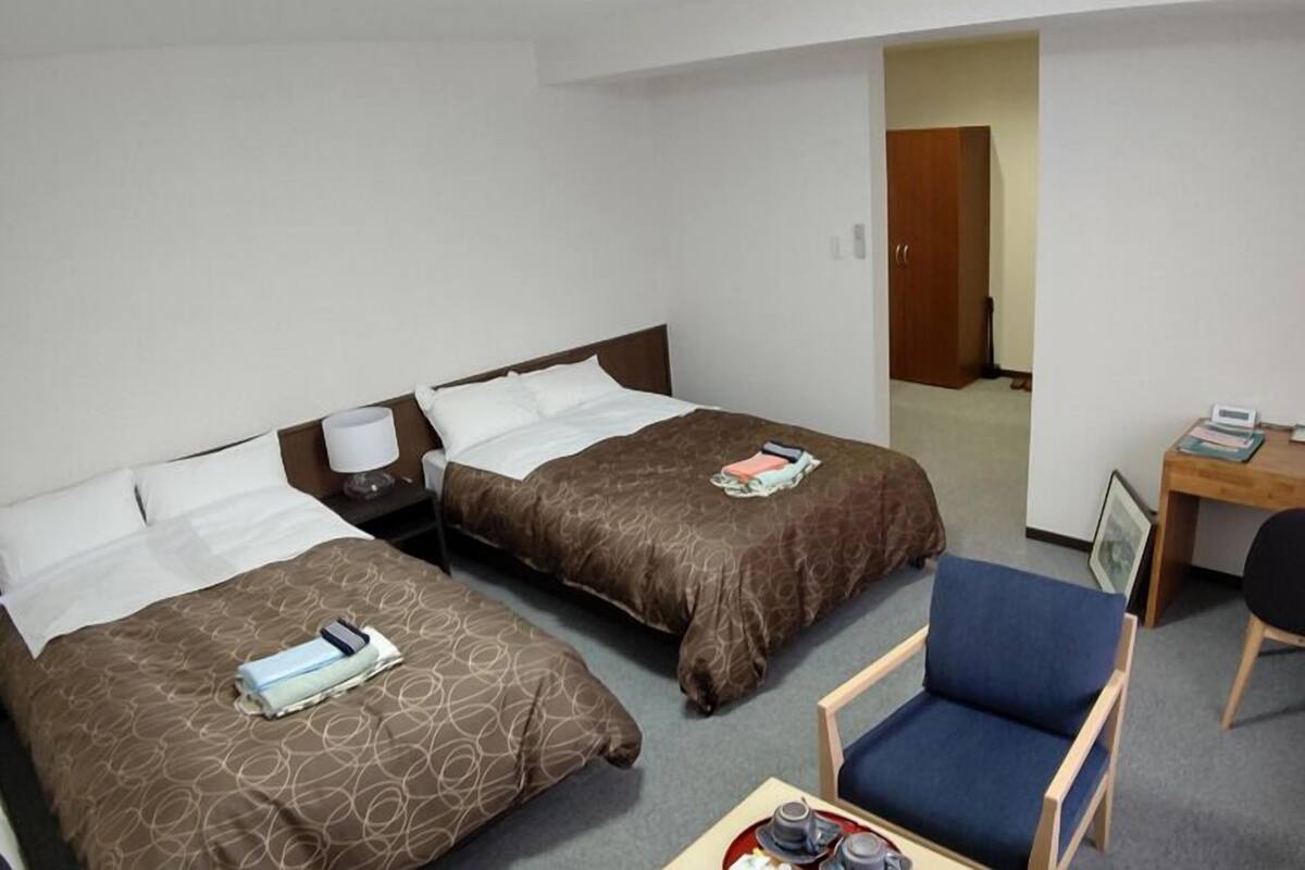 A hotel room with two beds, a desk, a chair, and a small table with a tray.