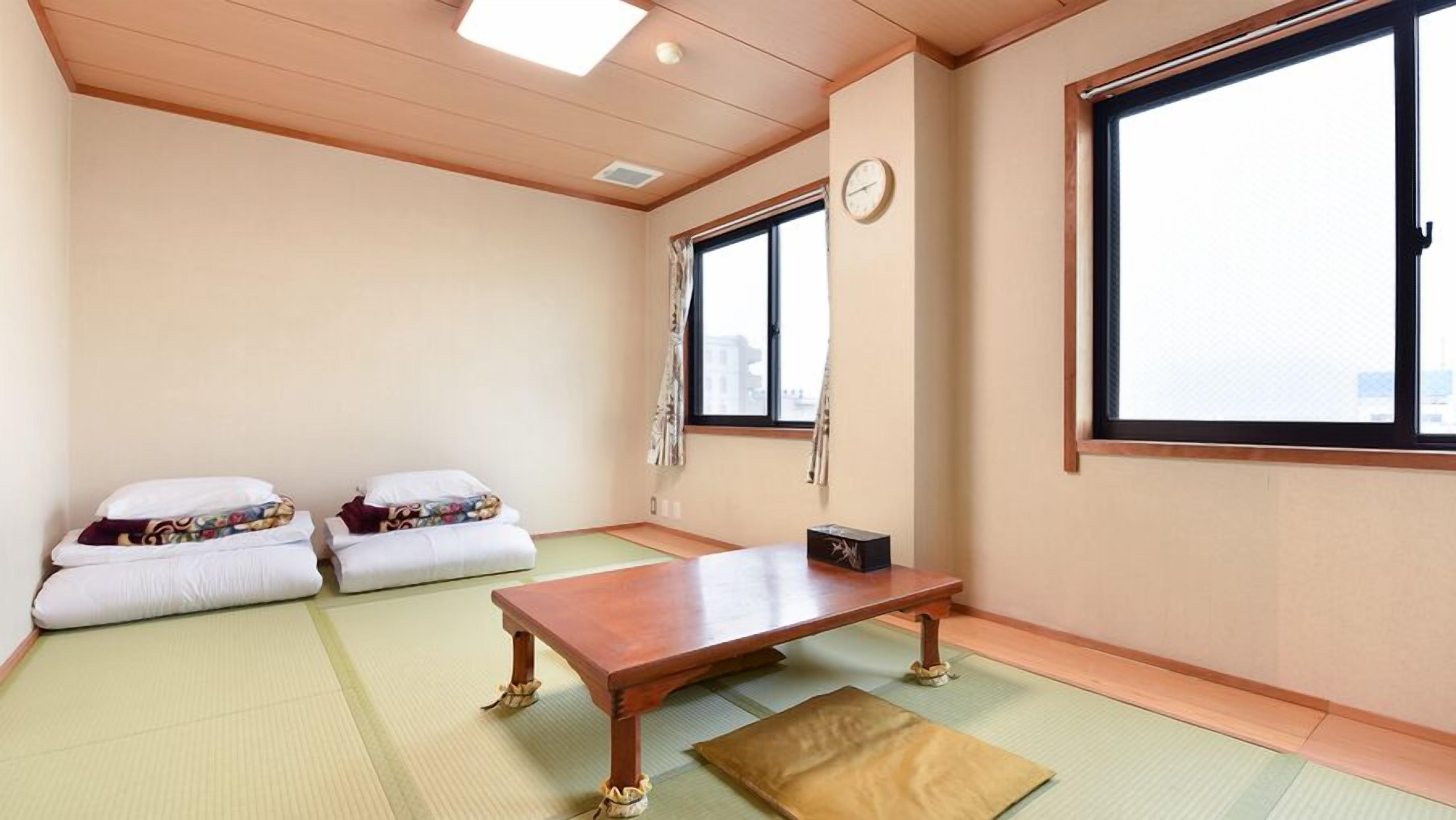 Een kamer met tatami matten, een houten tafel, twee kussens, een klok en een raam.