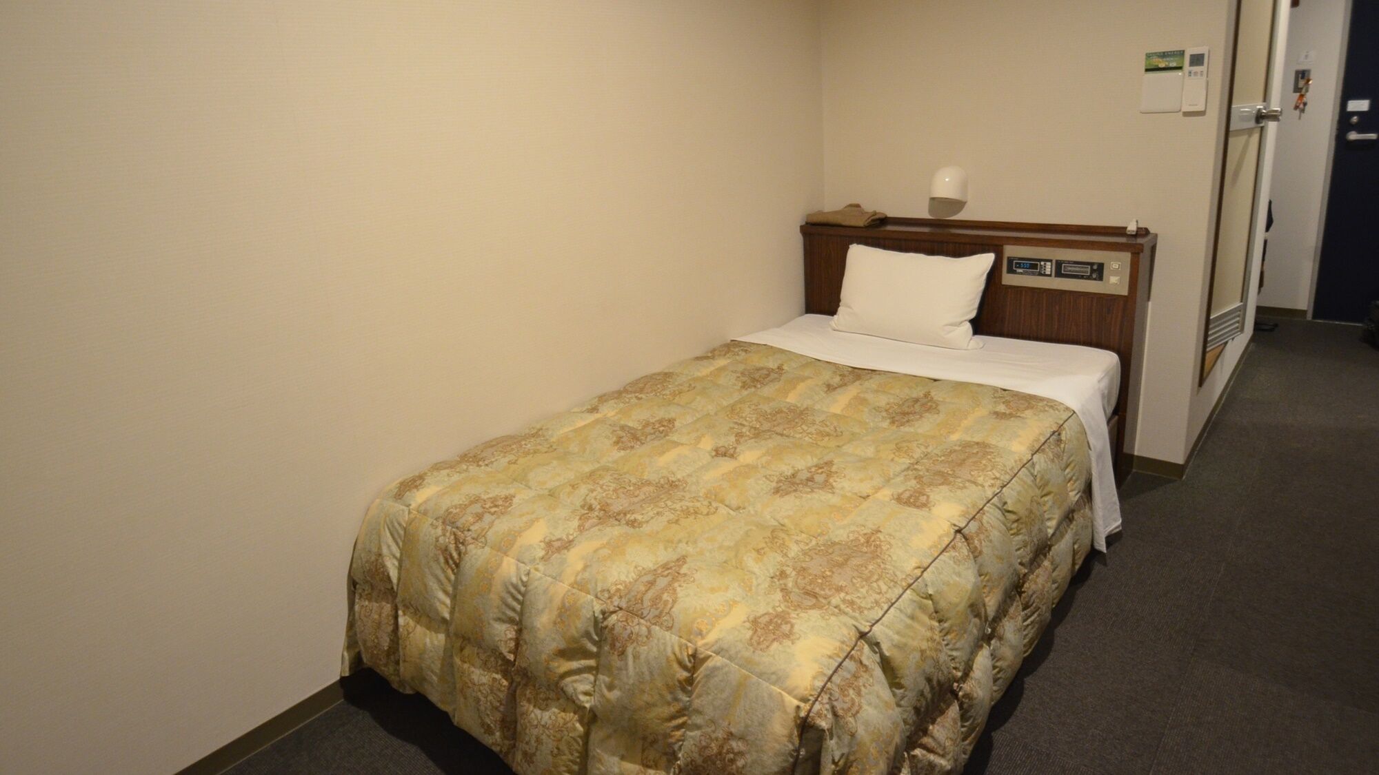 Une chambre d’hôtel avec un lit, une table de chevet, une horloge murale et une porte.