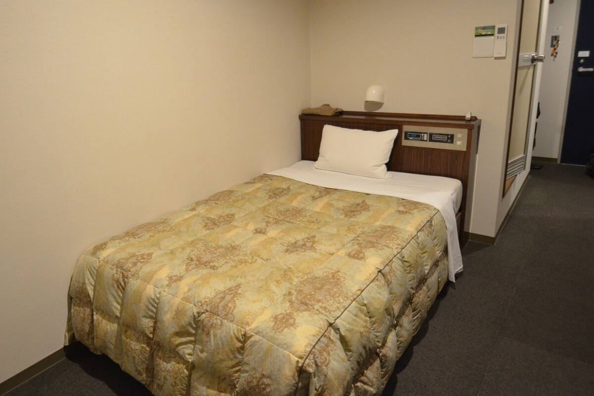 Ein Hotelzimmer mit Bett, Nachttisch, Wanduhr und Tür.