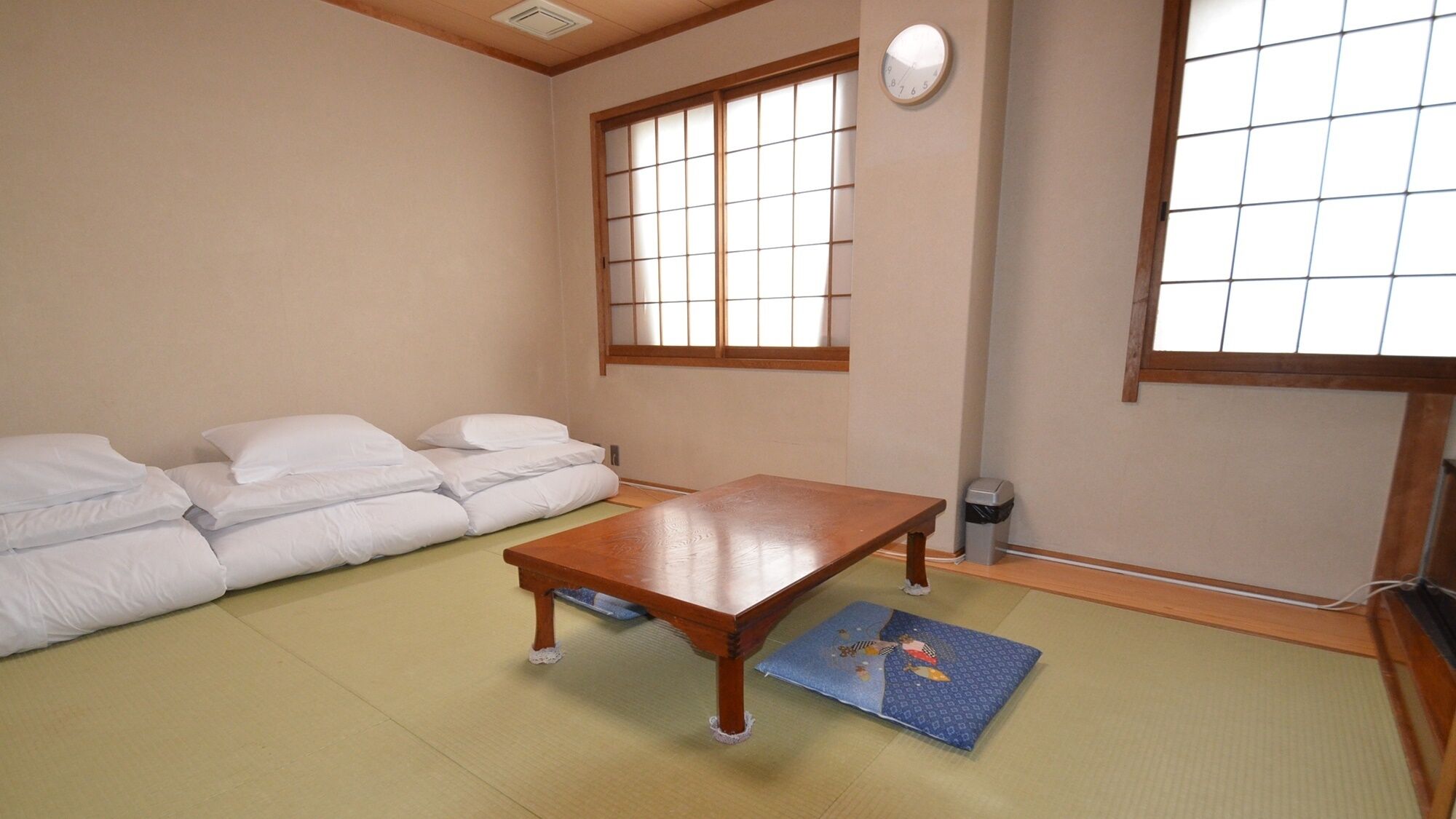Une pièce de style japonais traditionnel, avec un sol recouvert de tatamis, une basse table en bois, un canapé doté de coussins blancs et des portes coulissantes en papier de riz (shoji).