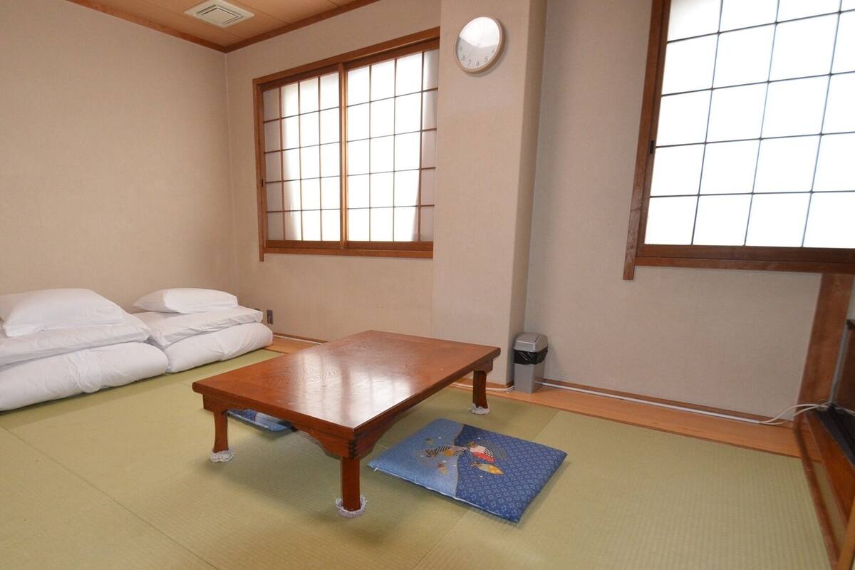 Ein traditioneller japanischer Raum mit Tatami-Boden, einem niedrigen Holztisch, einer weißen Couch mit Kissen und verschiebbaren Shoji-Schiebetüren.