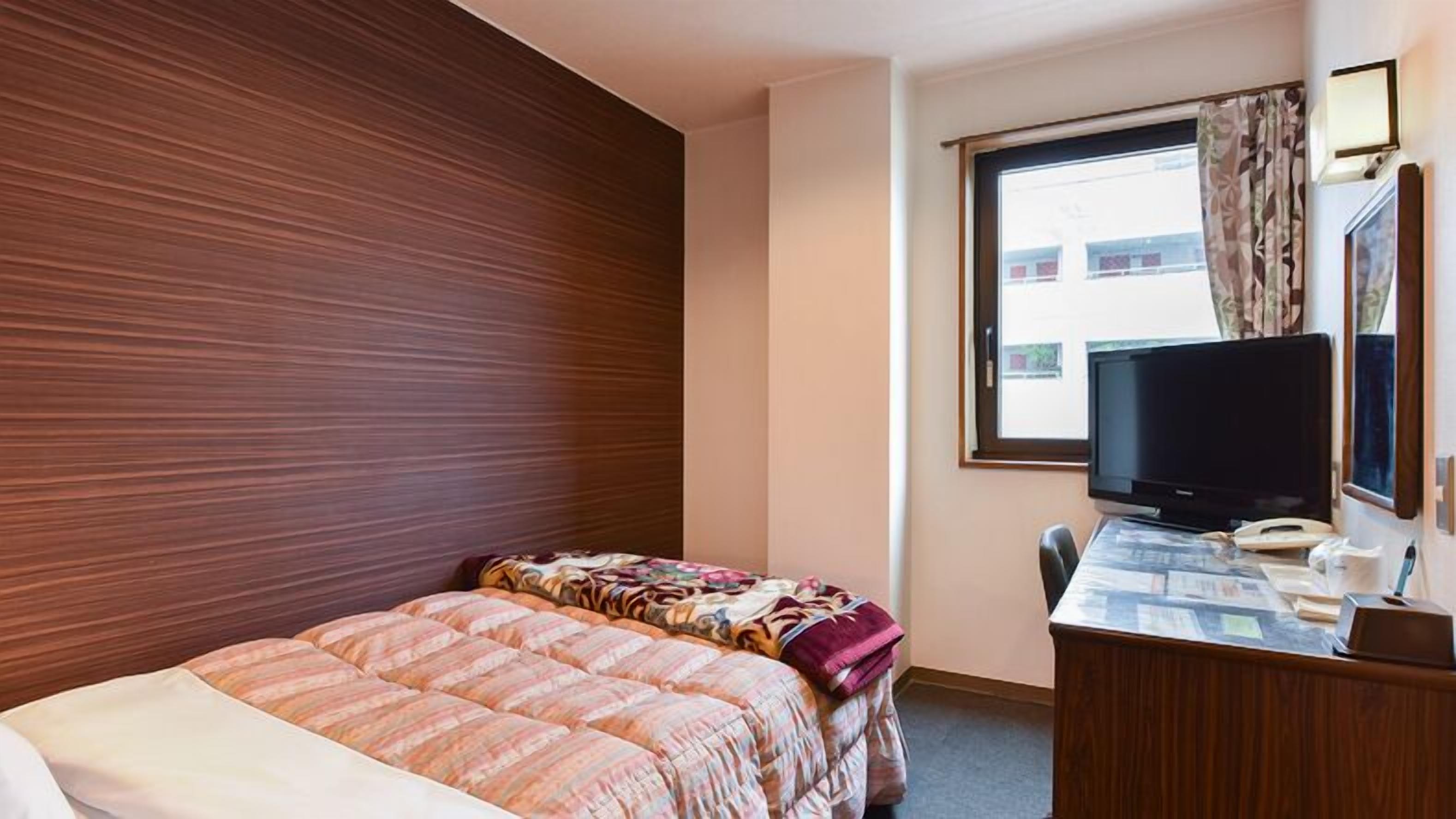 Een hotelkamer met een bed, een bureau met een computer, een televisie en een raam met gordijnen.