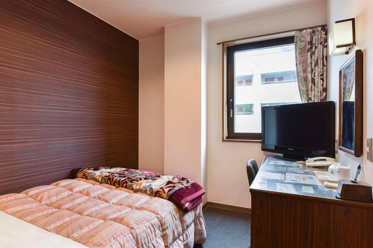 Ein Hotelzimmer mit Bett, Schreibtisch, Computer, Fernseher und einem Fenster mit Vorhängen.
