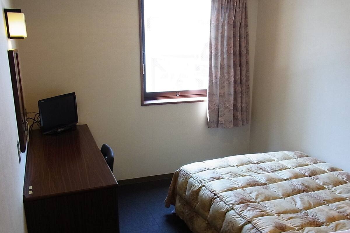 Ein schlichter, kleiner Raum mit einem Bett, einem Schreibtisch und einem Fenster.
