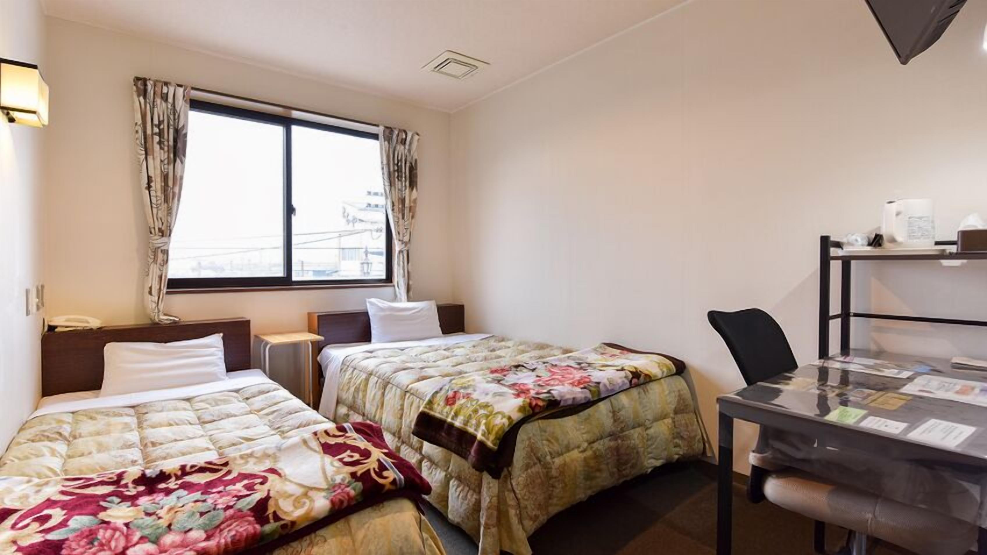Een hotelkamer met twee bedden, een bureau en een raam met gordijnen.