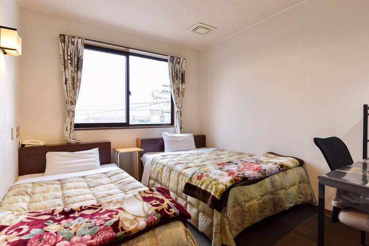 Ein Hotelzimmer mit zwei Betten, einem Schreibtisch und einem Fenster mit Vorhängen.