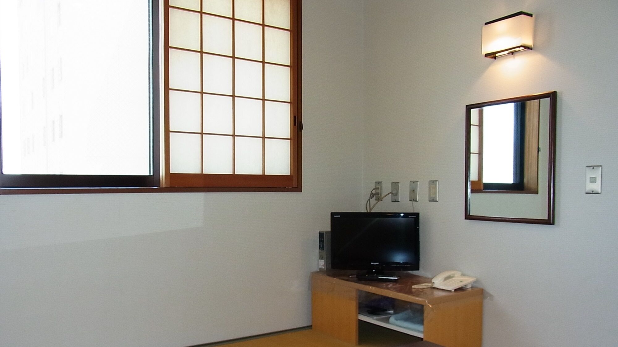 Une pièce avec un téléviseur posé sur un meuble en bois, un miroir au mur et une grande fenêtre à carreaux.