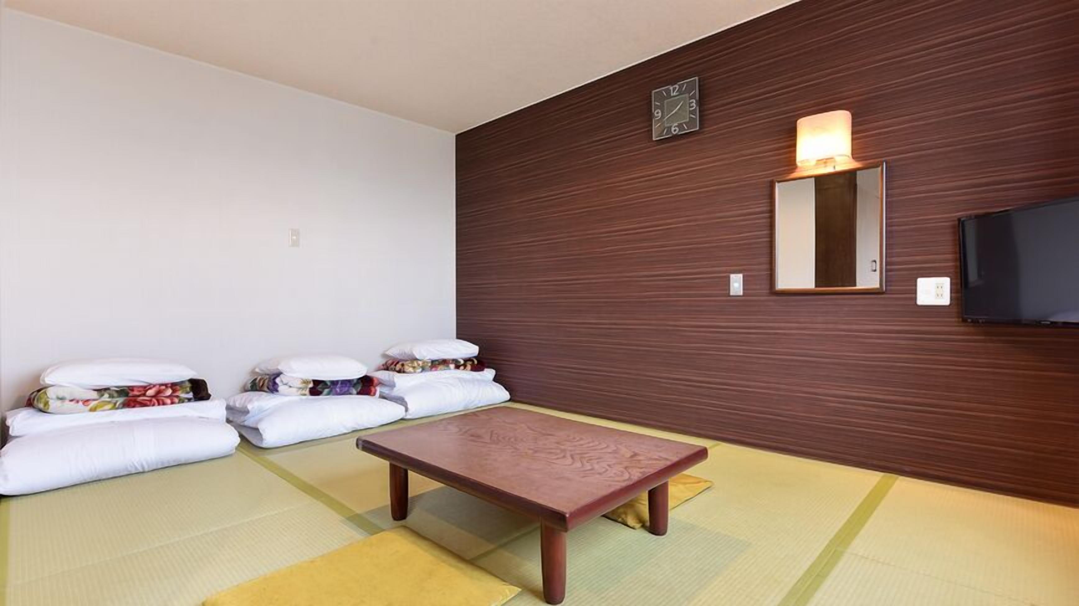 Een kamer met tatami vloerbedekking, een lage houten tafel en een aan de muur bevestigde televisie.
