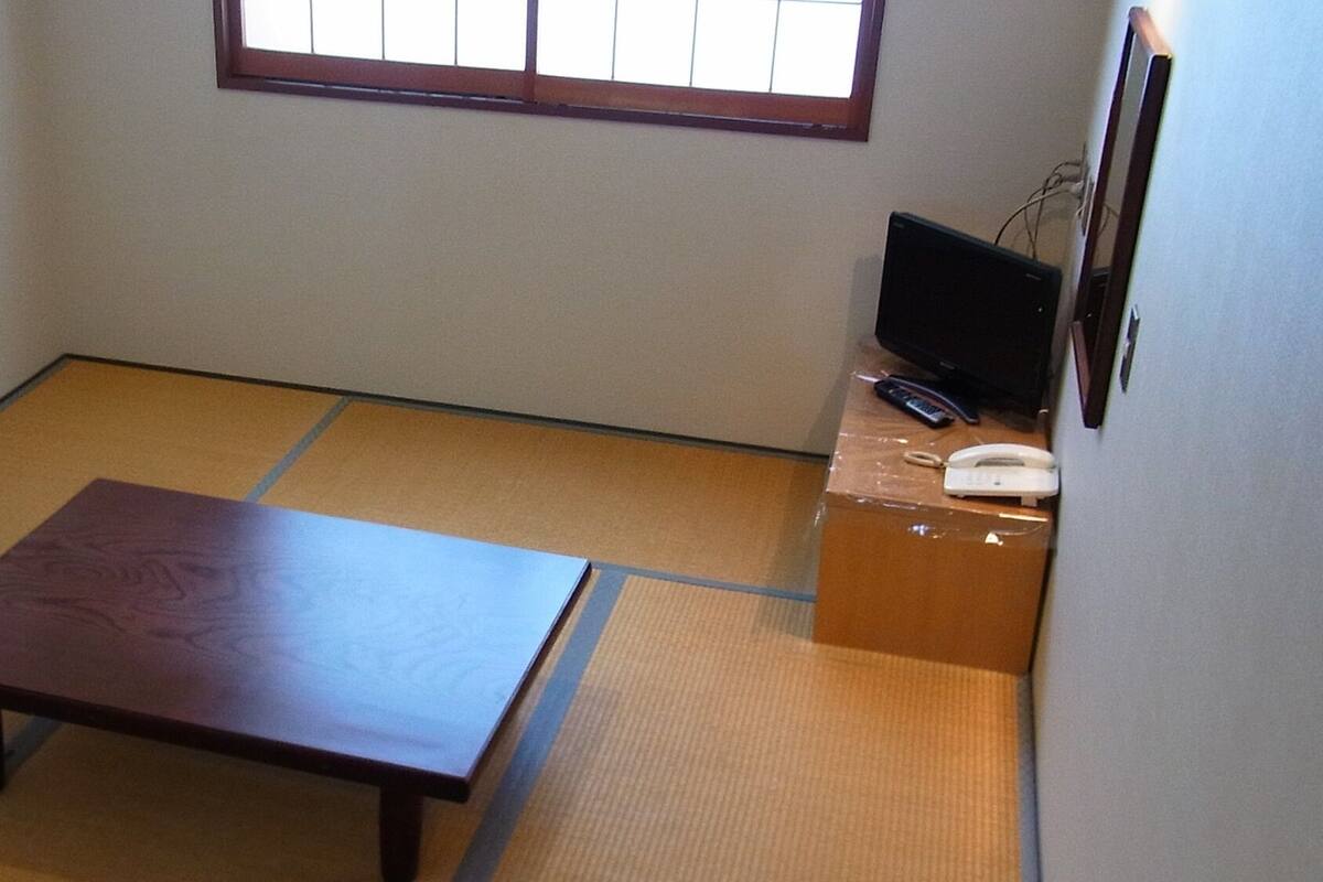 Ein Zimmer mit Tatami-Boden, einem niedrigen Holztisch, einem Fernseher auf einem Standfuß und einem Telefon.