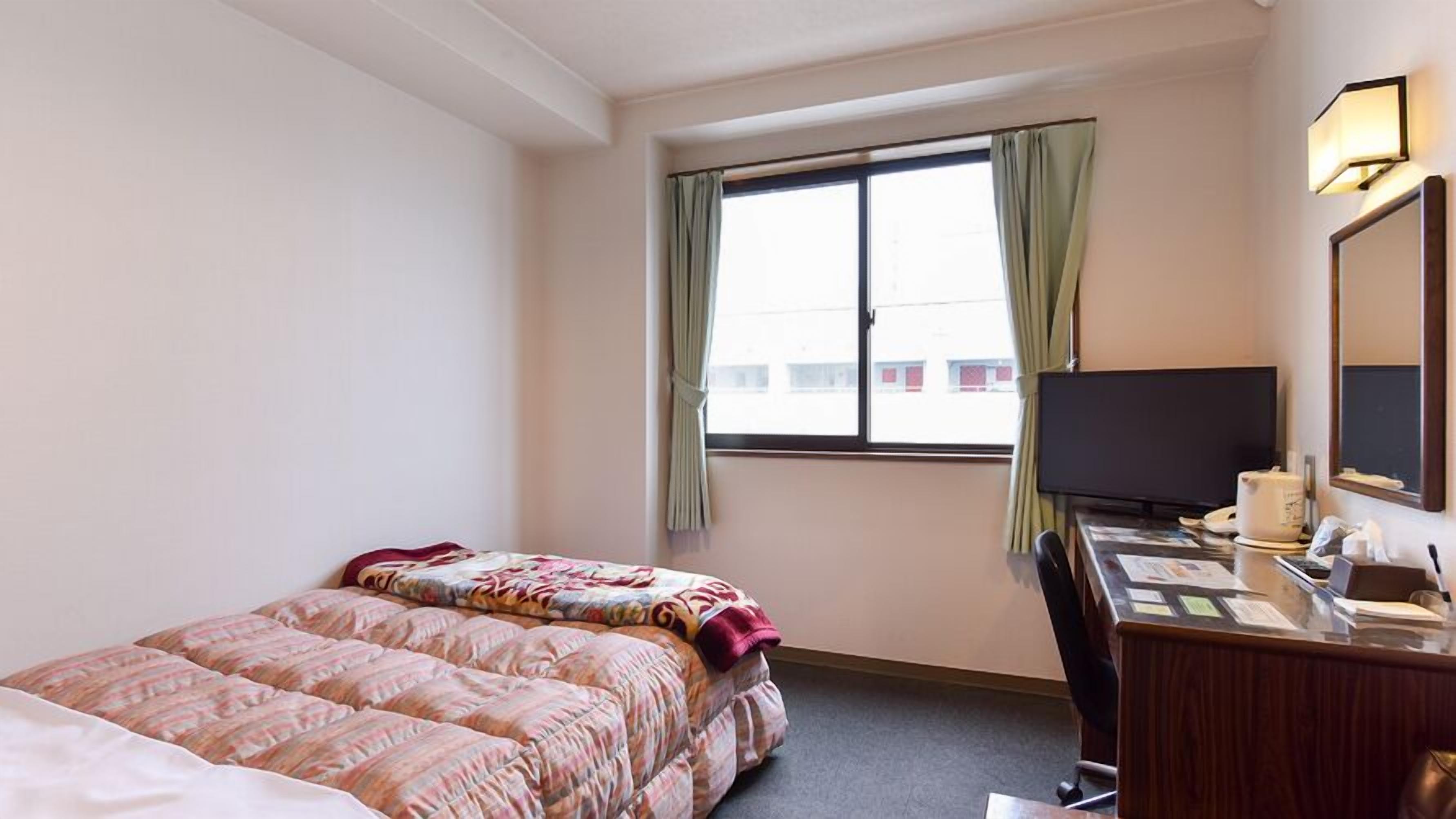 Hotelkamer met een bed, een bureau met computer, een televisie en een raam met gordijnen.