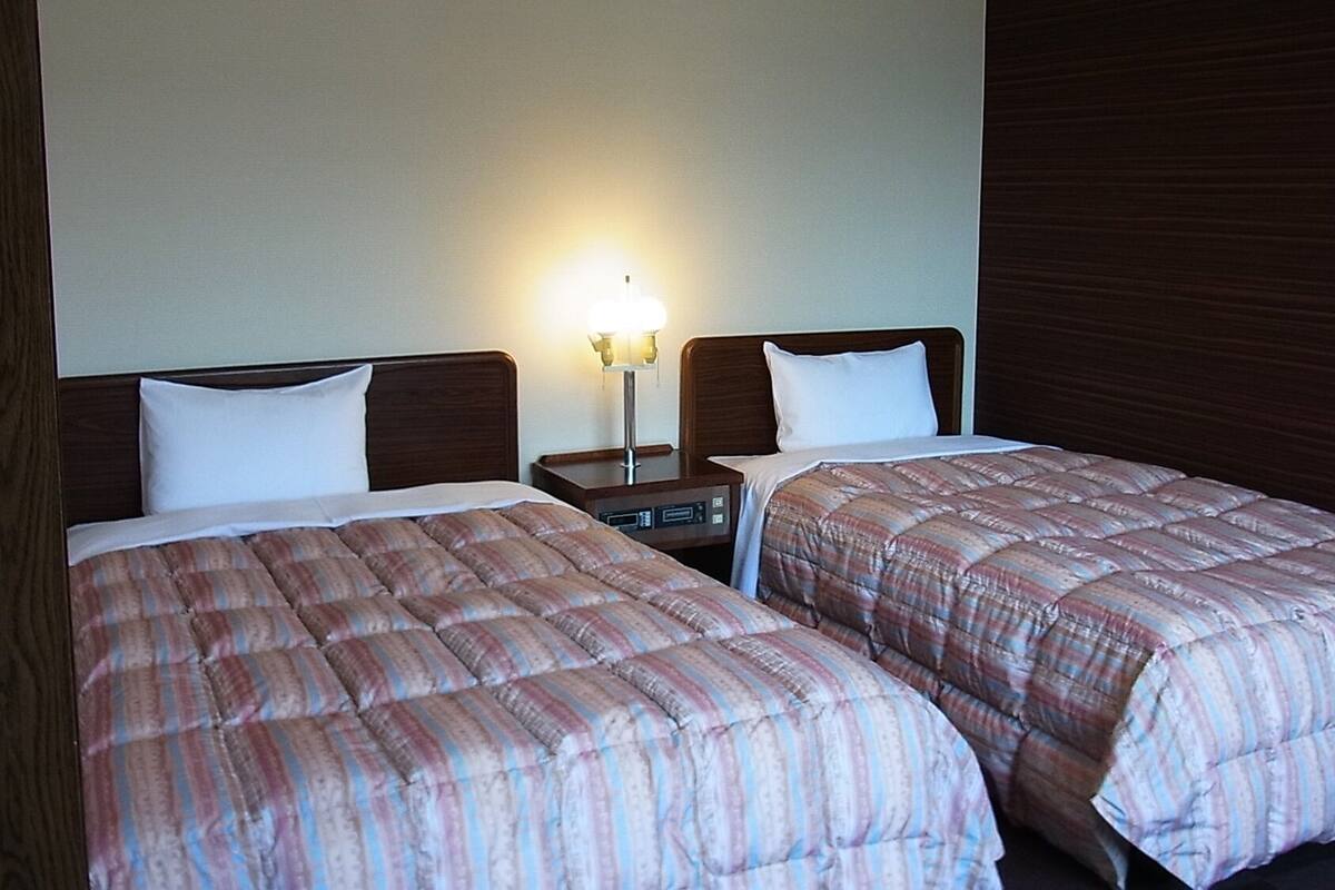 Zwei Betten mit gestreifter Bettwäsche, ein Nachttisch mit Lampe und ein hölzernes Kopfteil.