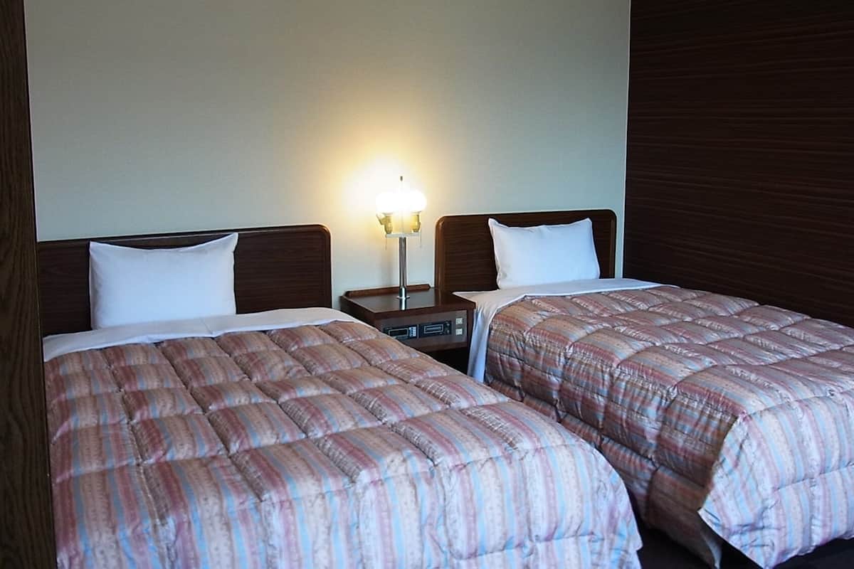 Dos camas con ropa de cama a rayas, una mesita de noche con lámpara y un cabecero de madera.