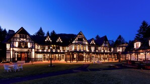 Hotel de estilo Tudor con una fachada bien iluminada, varias zonas de comedor y un patio cubierto de césped.