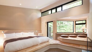 Un dormitorio moderno con una cama grande, bancos integrados y vistas a zonas verdes a través de amplios ventanales.