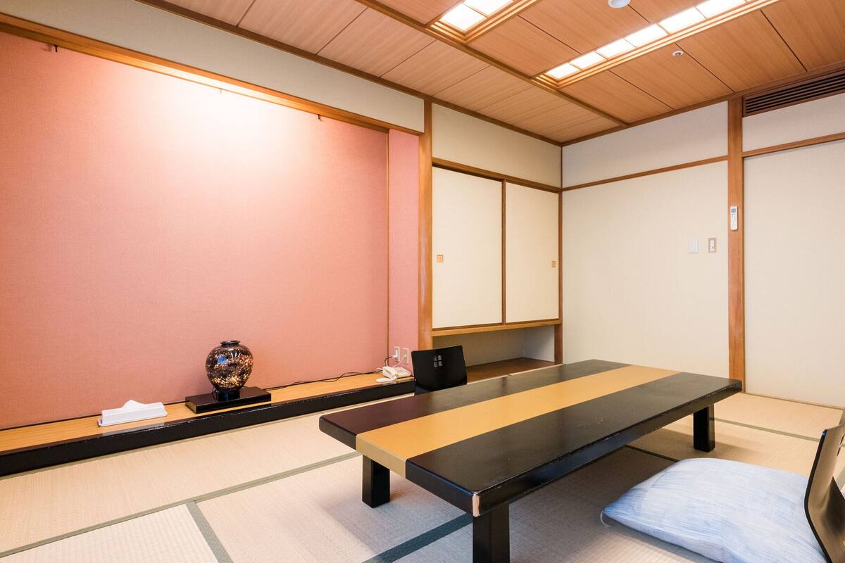 Um quarto japonês tradicional com esteiras de tatame, uma mesa baixa e um assento acolchoado.