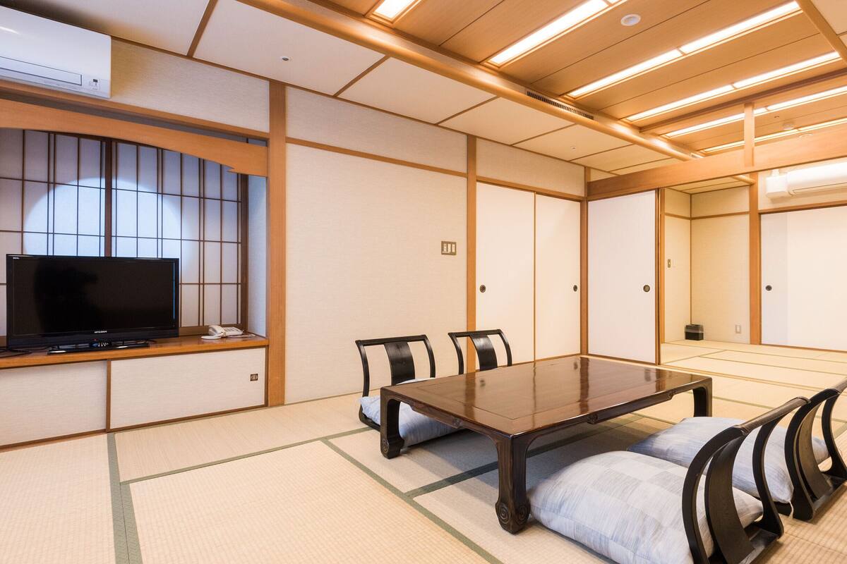 Uma sala de reuniões tradicional japonesa com tatames, uma mesa baixa e cadeiras pretas.