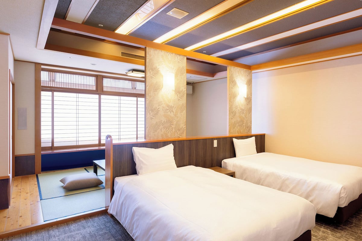 Quarto de hotel com duas camas, uma janela grande com persianas e teto no estilo tradicional japonês.