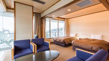 A hotel room with two beds, a seating area with a table, and large windows offering a city view.