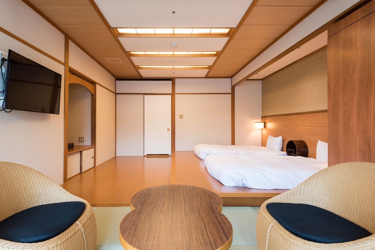 Quarto de hotel com cama, duas cadeiras de vime, televisão e guarda-roupa de madeira.