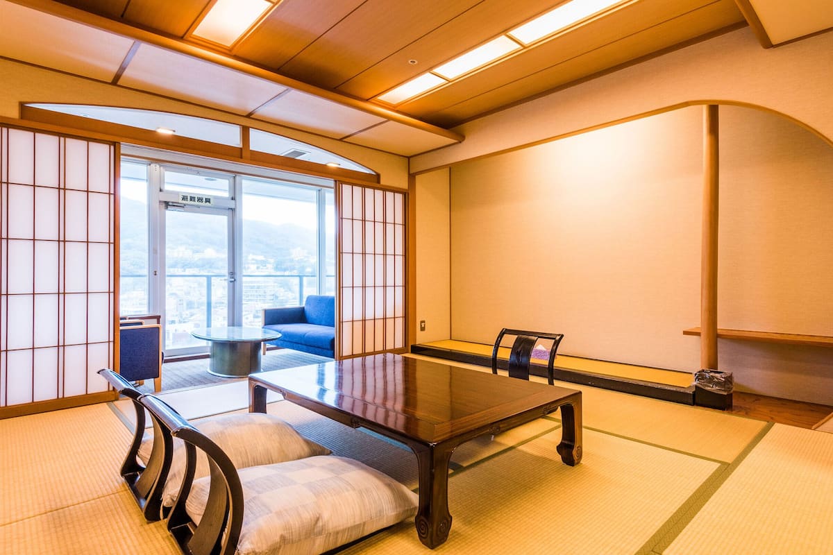 Uma sala de reuniões tradicional japonesa com piso de tatame, uma mesa baixa e vista através de uma porta de vidro.