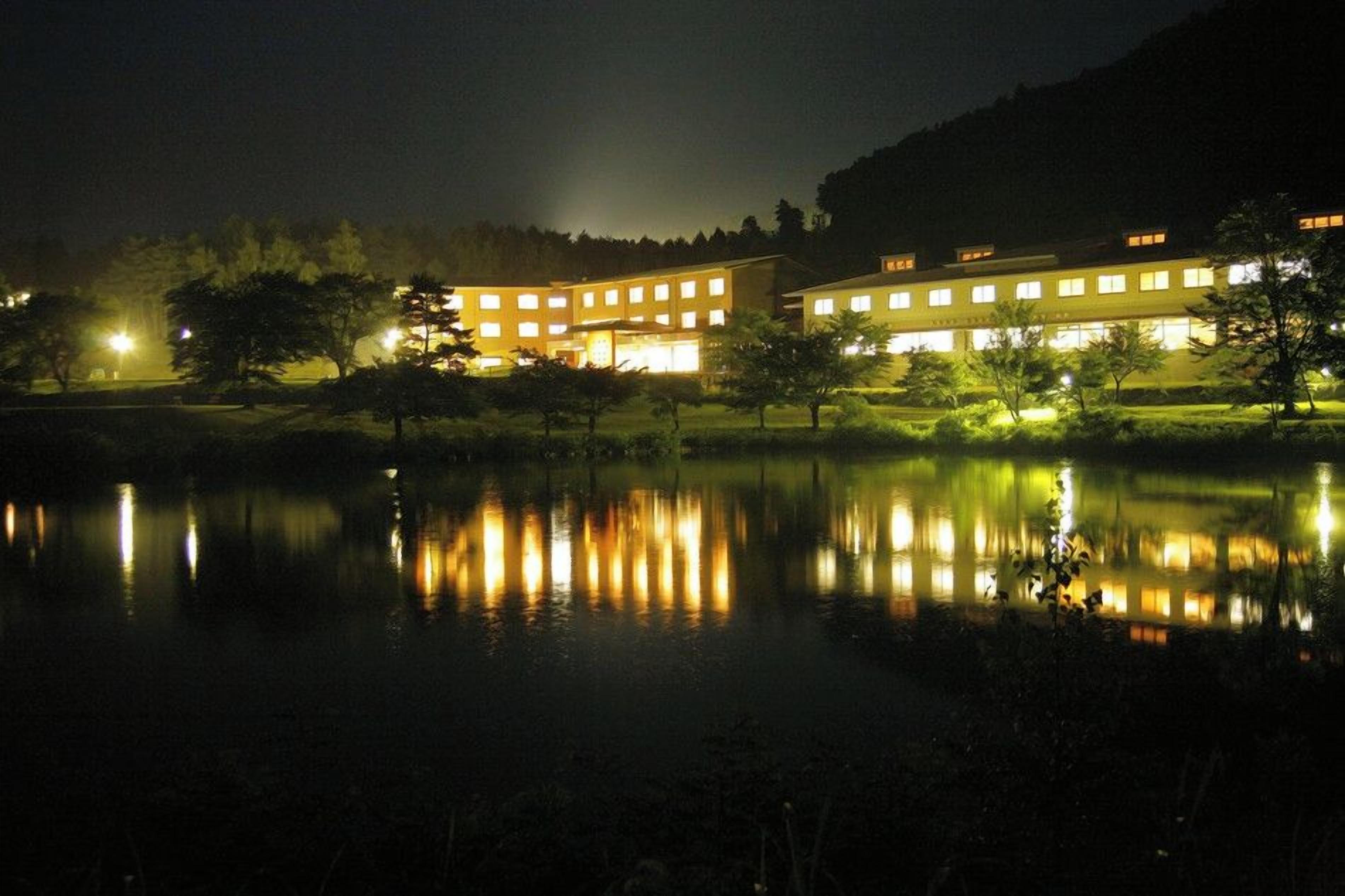 A building with multiple windows reflecting on a calm body of water at night.