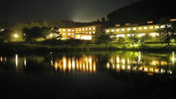 A building with multiple windows reflecting on a calm body of water at night.
