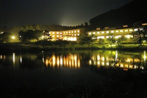 A building with multiple windows reflecting on a calm body of water at night. - Happoen Shika no Yu (Fujimi)