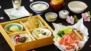 En traditionel japansk madkasse med forskellige retter, herunder ris, grøntsager og kød, samt små skåle og en kop.